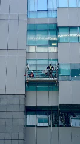 Professional high rise window cleaning service workers in gondola. Two workers use specialized equipment to access and clean windows of skyscraper as preventative maintenance and repair measure.
