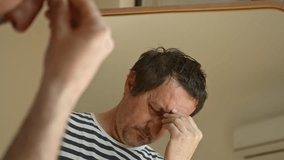 Mature man stands in front of mirror, looking at his reflection with deep regret, thoughtful and troubled expression at home. 4K with selective focus. - Powered by Shutterstock - Get 15% off with code: PIKWIZARD15