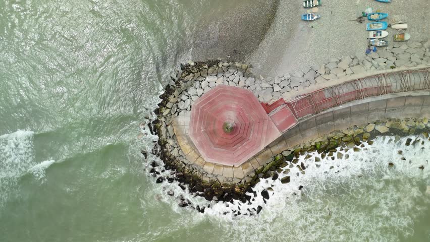 Beautiful coastal Mirador de La Punta in La Punta - restaurant built on a stone jetty, Lima, waves crashing and small fishing boats resting on the pebble beach - A top-down aerial parallax