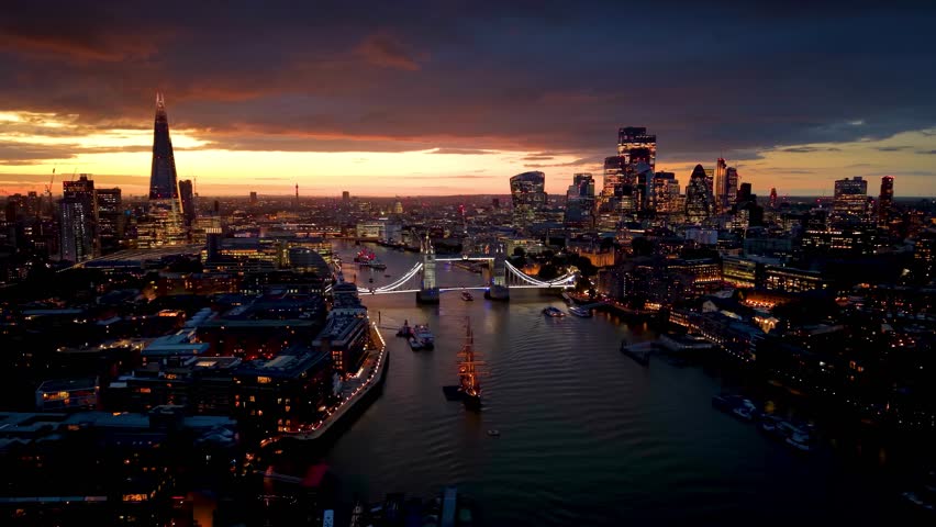 Beautiful, aerial evening view of the illuminated, urban skyline of London with Tower Bridge, River Thames boat traffic and City skyscrapers