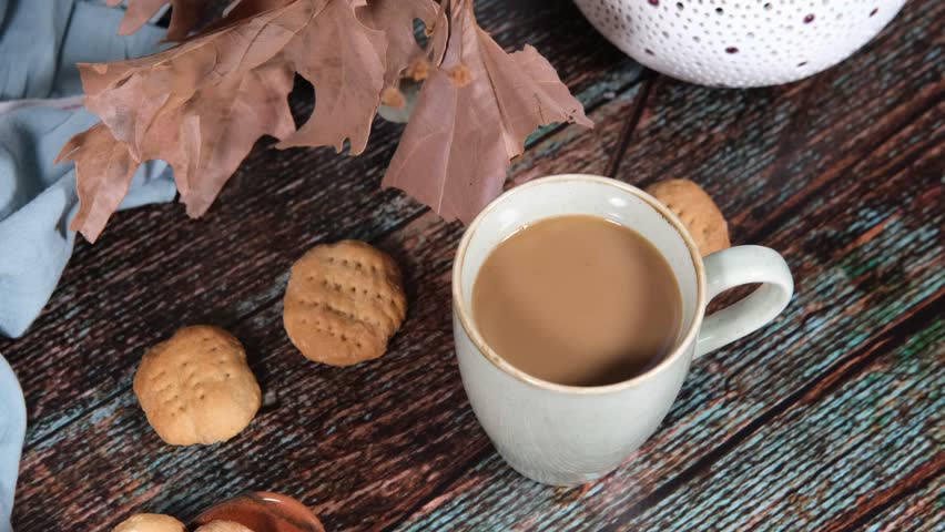 hot drink in blue mug with homemade cookies, dry leaves decoration, fall autumn vibes, rustic cozy seasonal mood