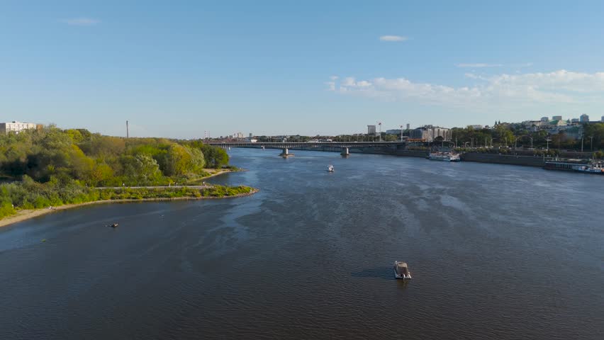 Aerial view of the Vistula River flowing under a bridge, with lush green trees on either side creating a scenic contrast, Warsaw, Poland.