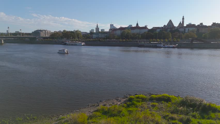 Aerial view of the Vistula River reflecting the clear sky, with the Warsaw skyline and historic buildings gracing the horizon, Warsaw, Poland.