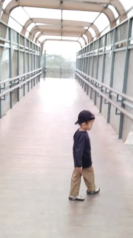 Asian boy in casual clothes and wearing a black hat, walking on a pedestrian bridge