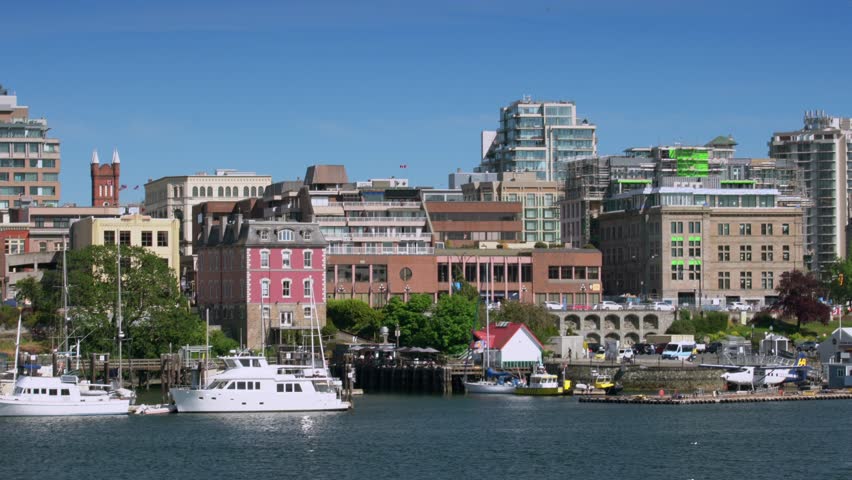 A vibrant waterfront cityscape with boats docked in the harbor, colorful buildings, and modern architecture under a clear blue sky.
