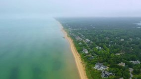 Scenic drone flyover of Cape Cod shoreline under foggy skies, with sandy beach, calm ocean waves, and coastal neighborhoods blending into mist-covered forest and horizon. - Powered by Shutterstock - Get 15% off with code: PIKWIZARD15
