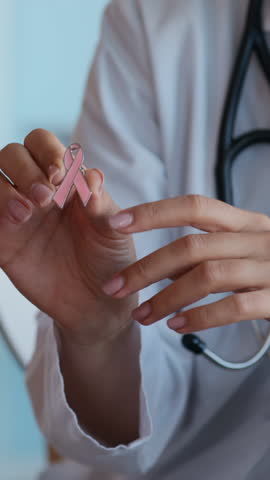 Vertical shot of anonymous therapist giving pink ribbon pin to female patient with breast cancer in hospital