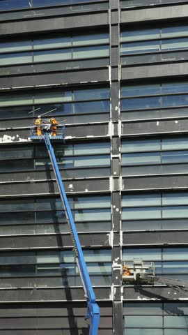 Construction Workers on Cherry Pickers Refurbishing High-Rise Building Facade.
Construction workers in safety gear operate cherry pickers to refurbish the exterior of a modern high-rise building. 