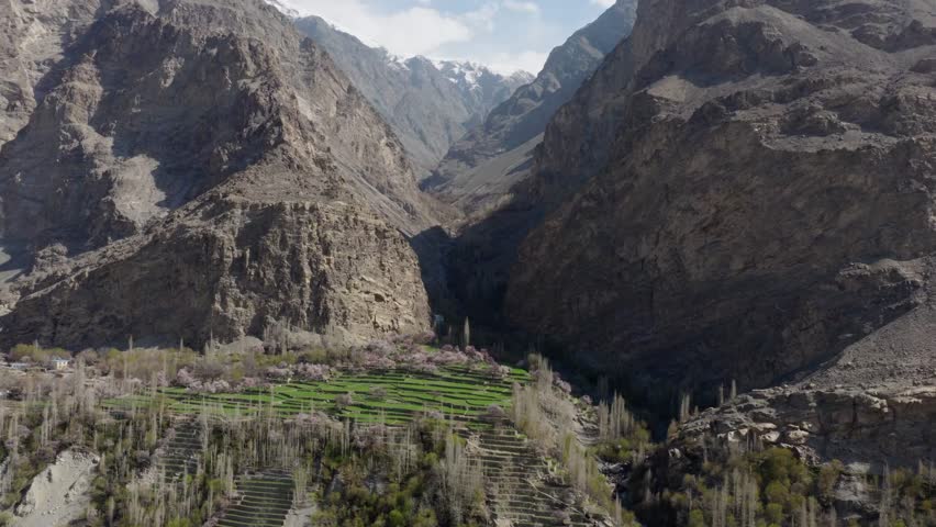 Aerial view of a serene valley in Pakistan, showcasing lush green terraces and towering mountains under a clear blue sky