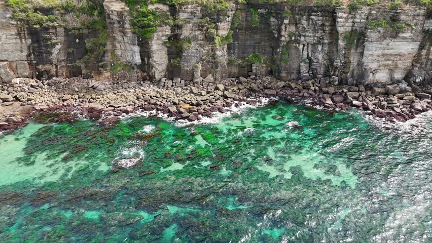 Aerial 4K drone footage of dramatic rocky cliffs meeting the turquoise Pacific Ocean on the New South Wales coast of Australia.