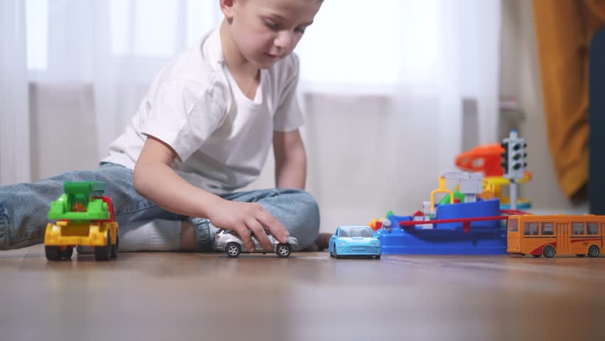 Young boy playing with toy cars. Child plays with a toy car. A boy is playing with toys in a car at home. A little boy engaged in play with lifestyle toy vehicles.