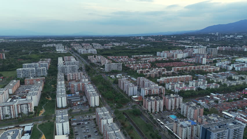 Drone video of Valle del Lili in Cali, showcasing sprawling urban cityscape under a serene twilight sky. The horizon reveals mountain silhouettes, emphasizing the city's expansive layout.
