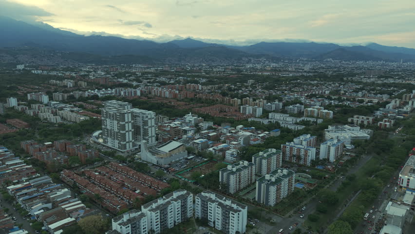 Aerial footage of Cali, Valle del Cauca, captures stunning cityscape with buildings, sunset lighting, and distant mountains. The urban landscape offers a mesmerizing aerial perspective.