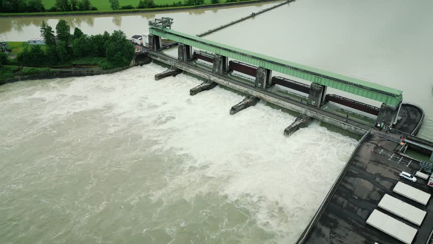 Hydroelectric water dam with opened full-flow relief gates, huge water stream flowing down. Drone flying over water dam on river Rhine in South Germany