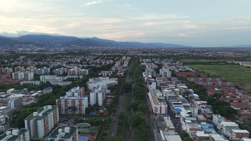 Aerial footage of Valle del Lili, Cali with a sprawling urban landscape and majestic mountains at dusk. The vast cityscape is bathed in soft, evening light, emphasizing its tranquility.