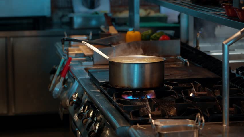 Essential process of cooking in a restaurant, showing a stainless steel pot boiling over a hot gas flame with steam rising, a fundamental step in food preparation