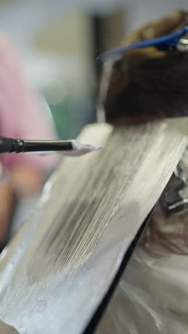 Close-up of a hairdresser applying dye to a client's hair with a comb. Women's procedures in a hairdresser's beauty and health.