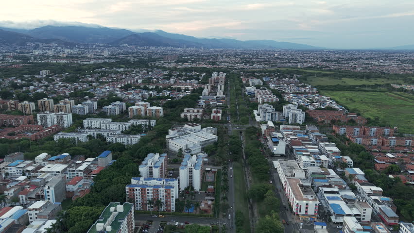 Drone footage over Valle del Lili in Valle del Cauca reveals an expansive urban landscape, showcasing residential and commercial areas under soft evening light, framed by distant mountains.