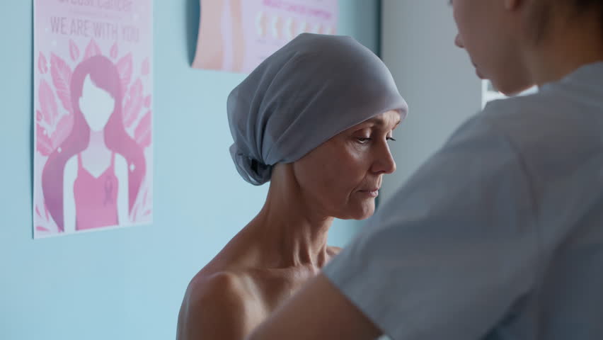 Medium close up shot of young Caucasian doctor in uniform palpating axillary lymph node of middle-aged woman with cancer in clinic