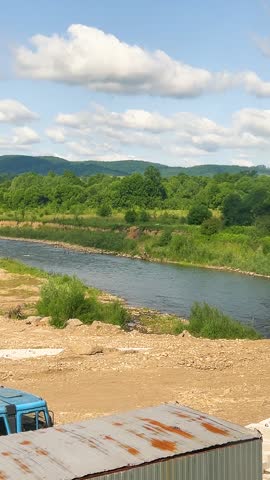 A train moves through the countryside against a backdrop of a river and trees. Vertical video.