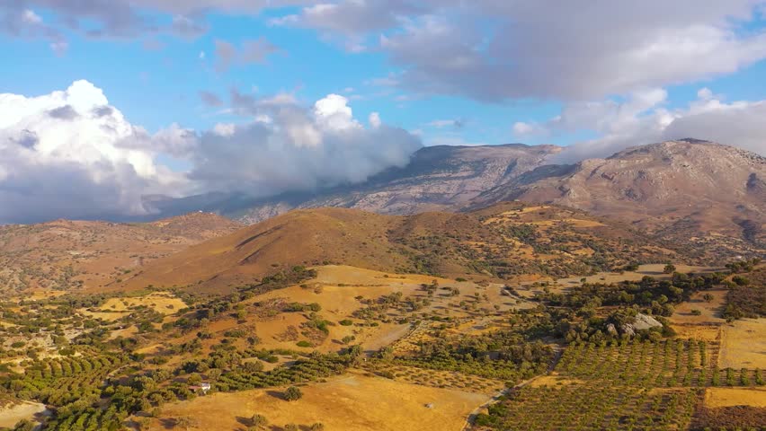 Aerial view of Crete, Greece, featuring mountains, olive groves, and a cloudy sky, highlighting Mediterranean landscapes and natural beauty.