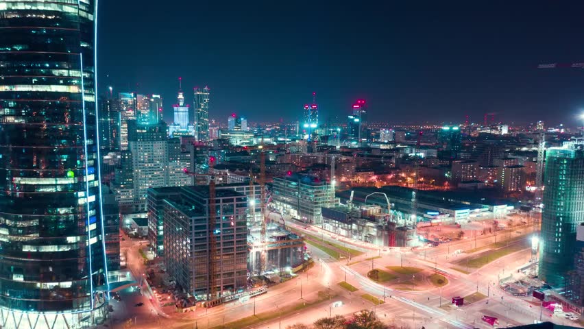 Aerial hyperlapse of Warsaw’s business center at night, featuring skyscrapers and the Palace of Science, showcasing urban lights and modern architecture.