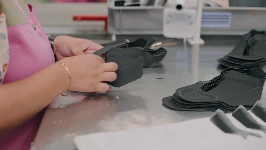 close up of worker hand cutting black leather shoe parts