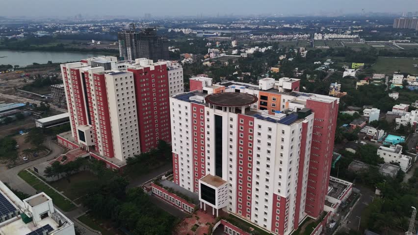 An aerial shot captures modern residential buildings with striking red and white facades. architectural details and rooftop features, including solar panels and a helipad, urban development Chennai