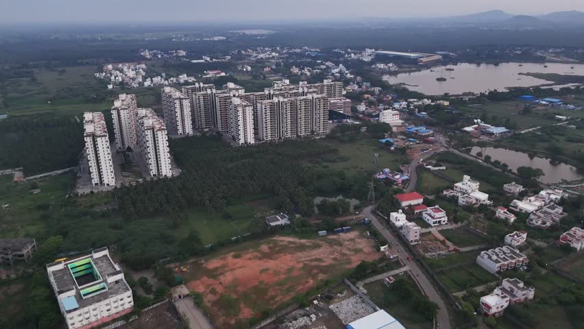 A wide shot of an urban landscape, highlighting city expansion with new construction. dense residential buildings coexisting with a more rural landscape, scattered homes, and a body of water.