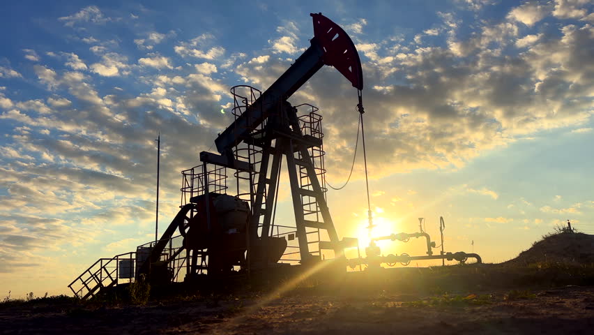 Oil Pump Jack Operates on Beautiful Sunset at Oil Field in Industrial Area. Crude pump jack working on sunrise in oil field. Oil drill rig, drilling derrick in oilfield. Crude petroleum industry. 