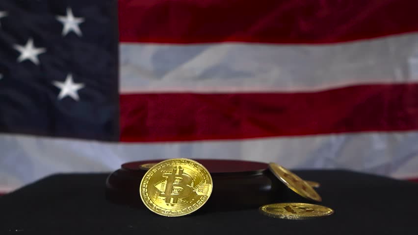 Slow motion video of a justice court hammer or gaol hitting a wooden board while golden shiny bitcoin money cryptocurrency coins are on the side, flying and bouncing from the impact. American flag.