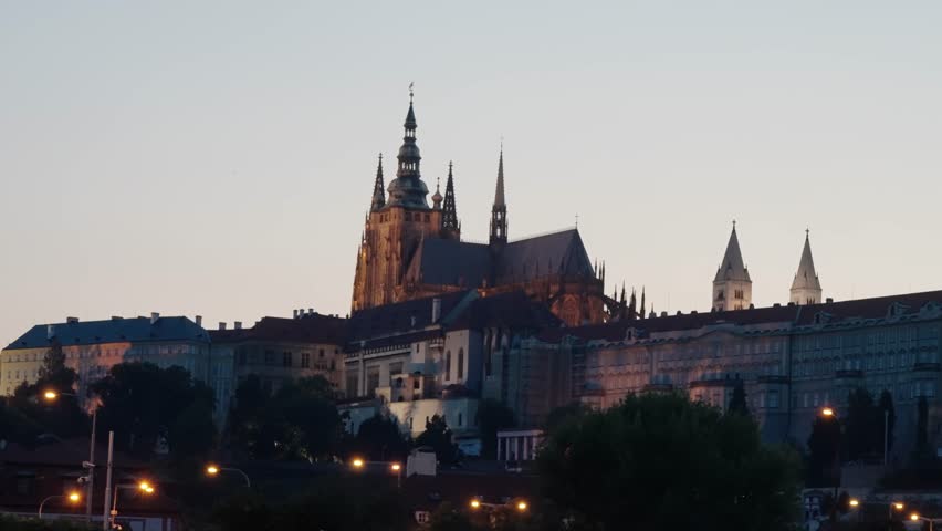 St. Vitus Cathedral and Prague Castle glow warmly under evening light as night begins in Prague, Czech Republic