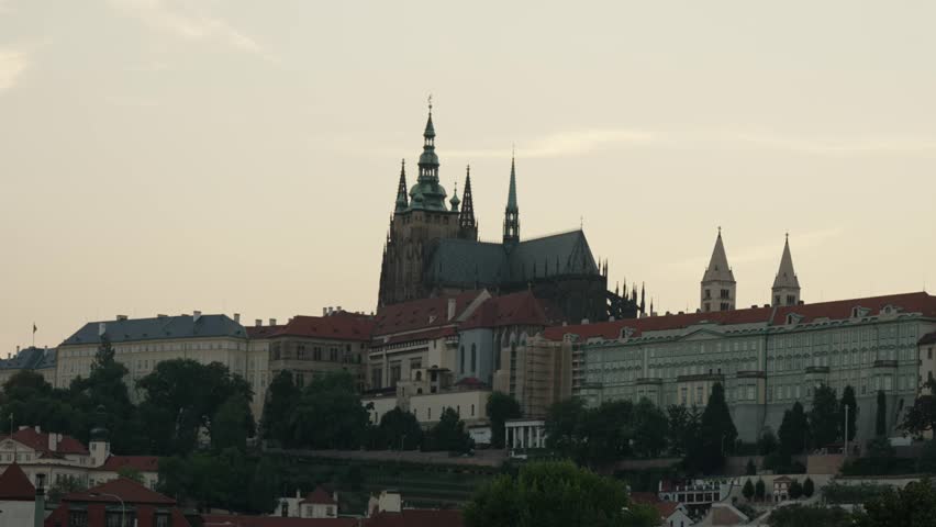View of Prague Castle and St. Vitus Cathedral at dusk, with historic rooftops and towers silhouetted against the evening sky