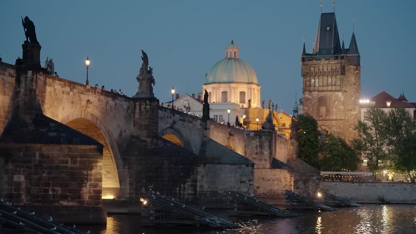 The Charles Bridge glows warmly with statues and the Old Town Bridge Tower lit under the night sky in Prague, Czech Republic