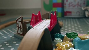 Close-up of a toy train moving down a wooden bridge with other colorful toys, including Lego blocks, scattered around the floor in a kids' room - Powered by Shutterstock - Get 15% off with code: PIKWIZARD15