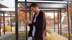 Man using smartphone in urban park setting, managing daily tasks with focus, surrounded by modern architecture and greenery, showcasing technology in everyday life - Powered by Shutterstock - Get 15% off with code: PIKWIZARD15