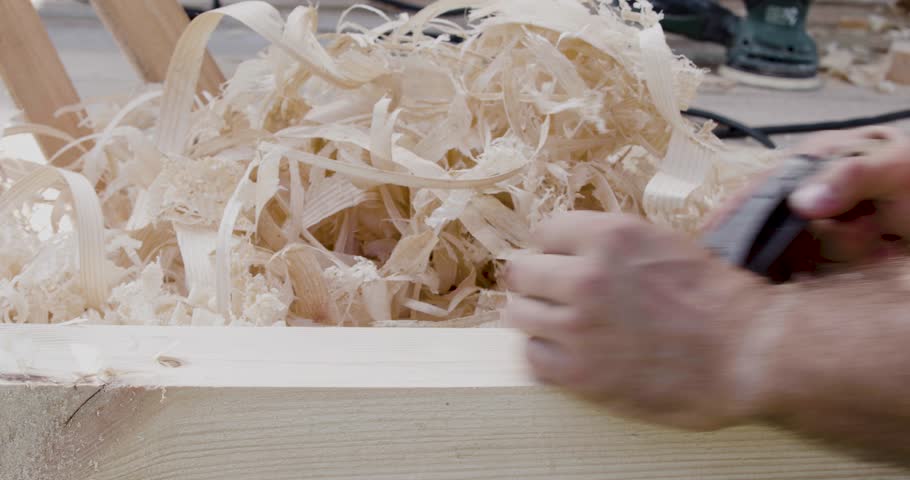Close-up of a carpenter's hands while working with a hand plane. Close view of a carpenter's hands refining wood edges with a hand plane, showing careful attention.