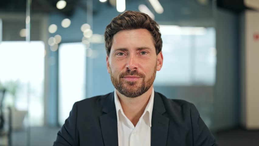 Confident businessman in a modern office, wearing a dark suit, speaks passionately during a video call. Expresses serious emotions while gesturing.