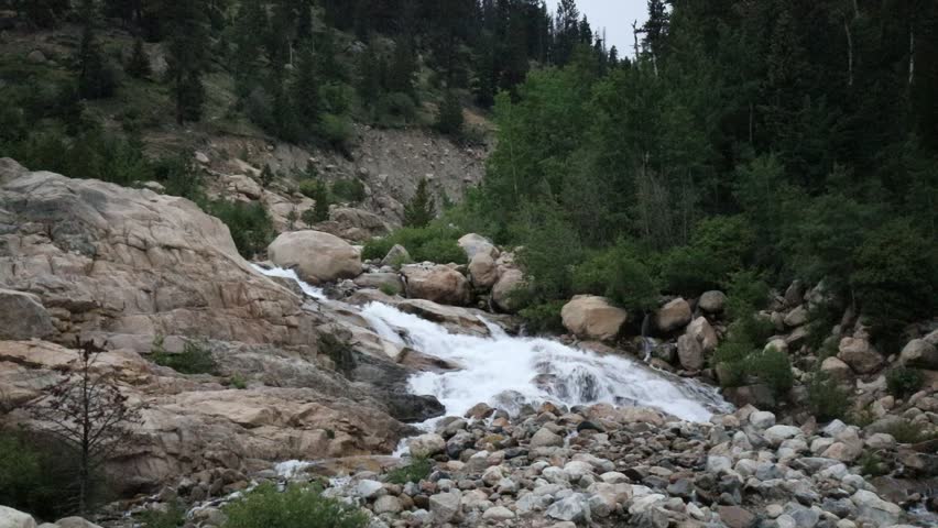 Snow melt in stream over rapids.  Alluvial Fan Falls in the Rockies in Colorado.  Green trees, boulders in the stream with whitewater rapids. Boulders, green trees and whitewater falls prior to flood.