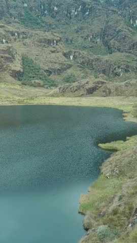 Peasant woman on a rock on the shore of a lagoon (Laguna Linda, Pachitea, Peru), peace, travel, tourism concept. VERTICAL VIDEO. DRONE