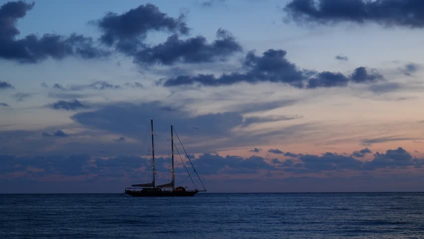 Oglaistro Marina, Italy. Blue hour seascape at Baia Arena, Ogliastro Marina Bay, Italy: calm Tyrrhenian waters and soft pastel clouds after sunset, with a two-masted sailing ship far on horizon. 4K.