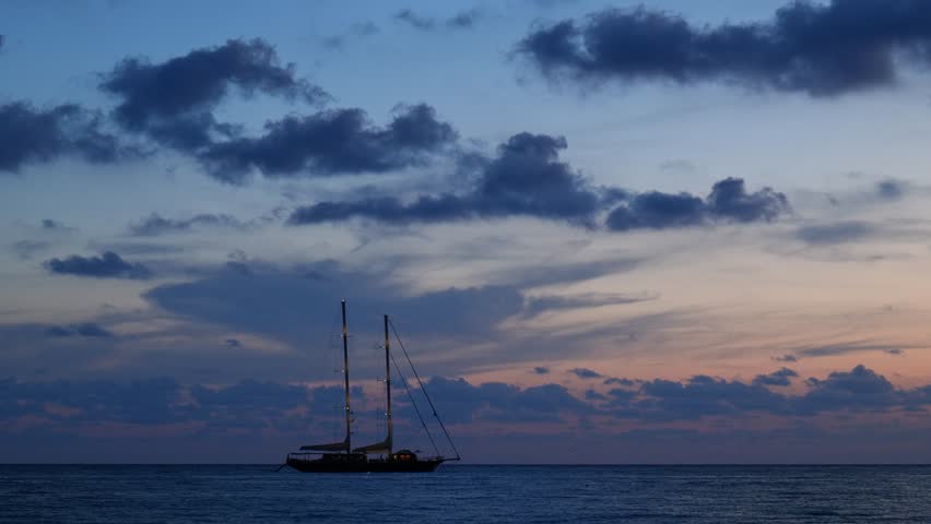 Ogliastro Marina, Italy. Blue hour seascape at Baia Arena, Ogliastro Marina Bay, Italy: calm Tyrrhenian waters and soft pastel clouds after sunset, with a two-masted sailing ship far on horizon. 4K.