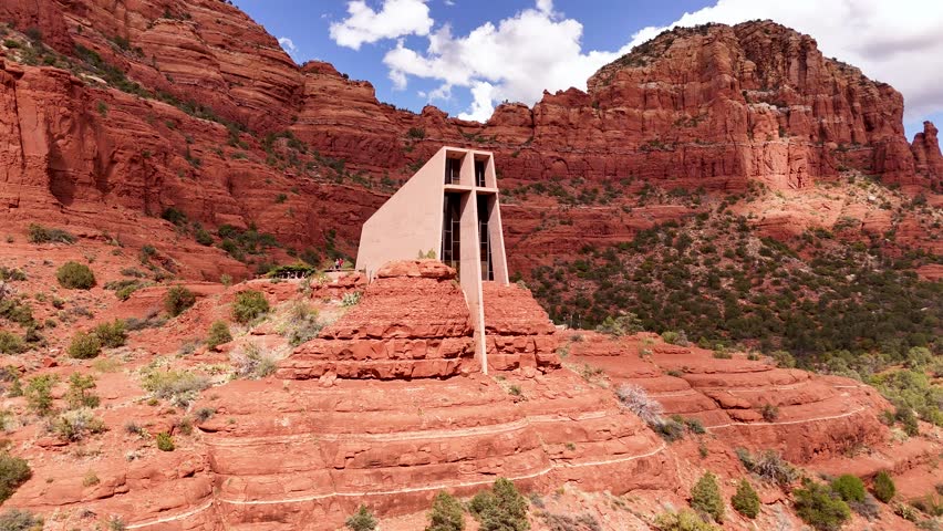 Aerial drone shot of the stunning Chapel of the Holy Cross in Sedona, Arizona. The unique architectural landmark is nestled within the famous red rock cliffs on a beautiful day.