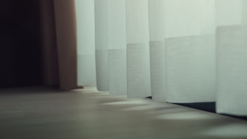 Soft sunlight shining through white sheer curtain swaying in the breeze, close-up of curtain fabric creating a warm minimalist interior scene with natural light and cozy atmosphere