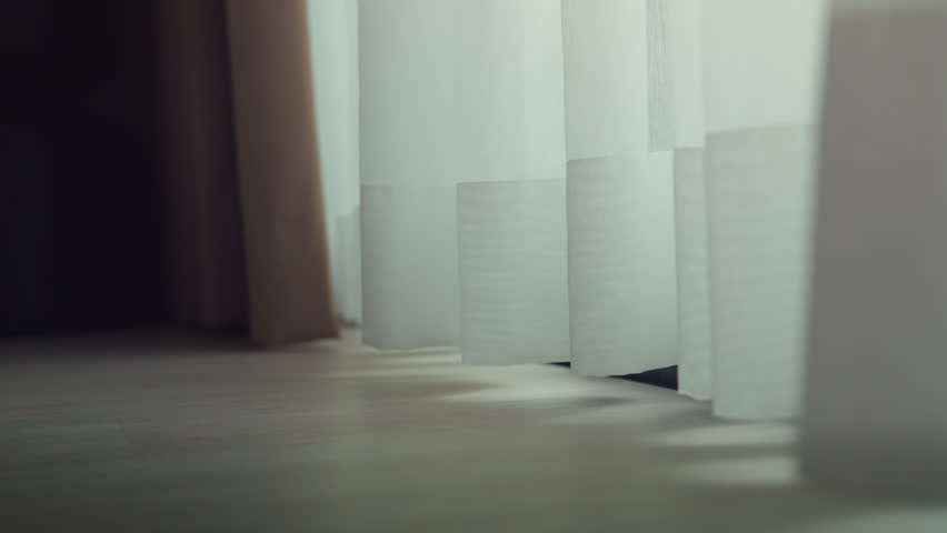 Soft sunlight shining through white sheer curtain swaying in the breeze, close-up of curtain fabric creating a warm minimalist interior scene with natural light and cozy atmosphere