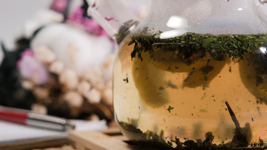 The process of brewing fresh loose leaf herbal tea with lemon in a glass teapot, rich flavor and aroma, close-up shot