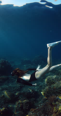 Woman freediving underwater on coral reef in Raja Ampat, vertical screen
