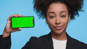 Young woman in black blazer holding smartphone with green screen while shaking her head in disapproval against blue background. - Powered by Shutterstock - Get 15% off with code: PIKWIZARD15