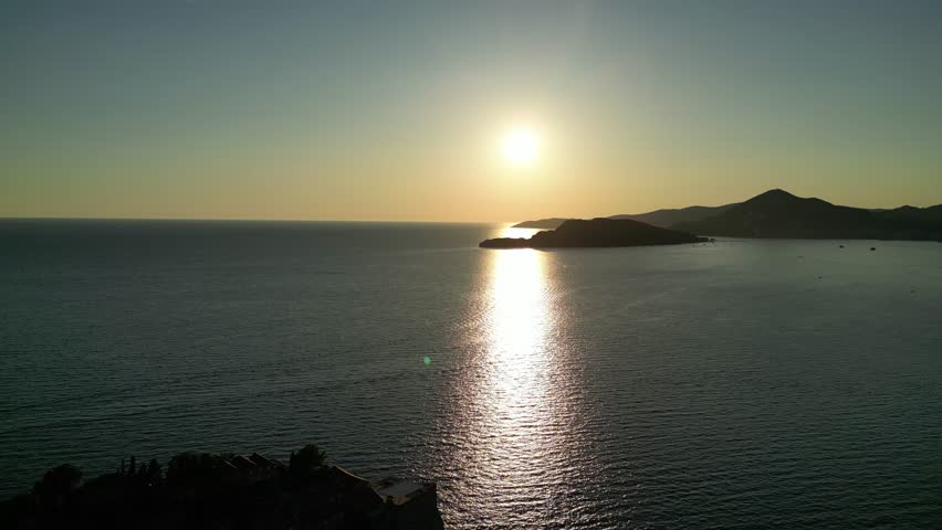 Aerial drone video of sunset over the Budva coastline in Montenegro. Golden reflections on the sea with mountains and islands in the distance. Perfect for travel, tourism, and motivational projects.