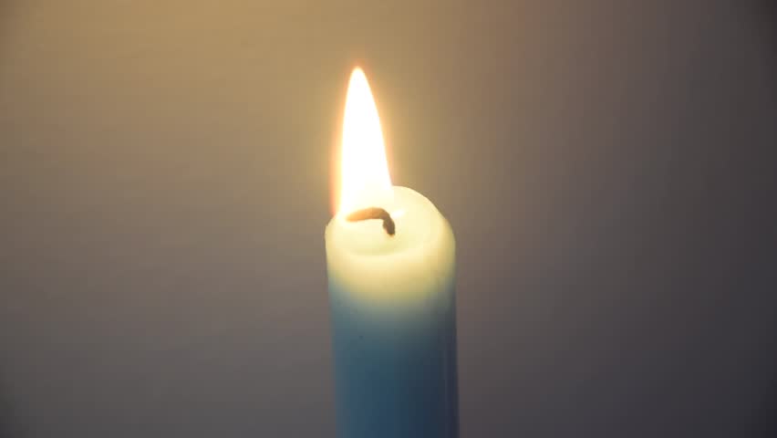 Close shot showing the flame of a clue candle with a white background, and the candle flame being blown out
